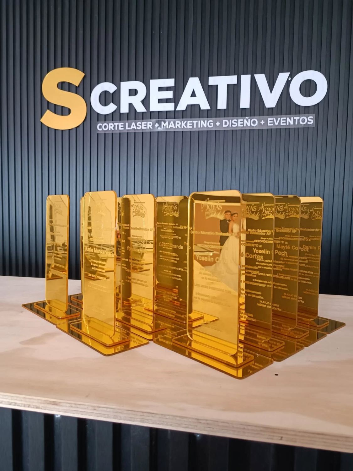 Reconocimientos en acrílico espejo dorado frente al letrero de Screativo